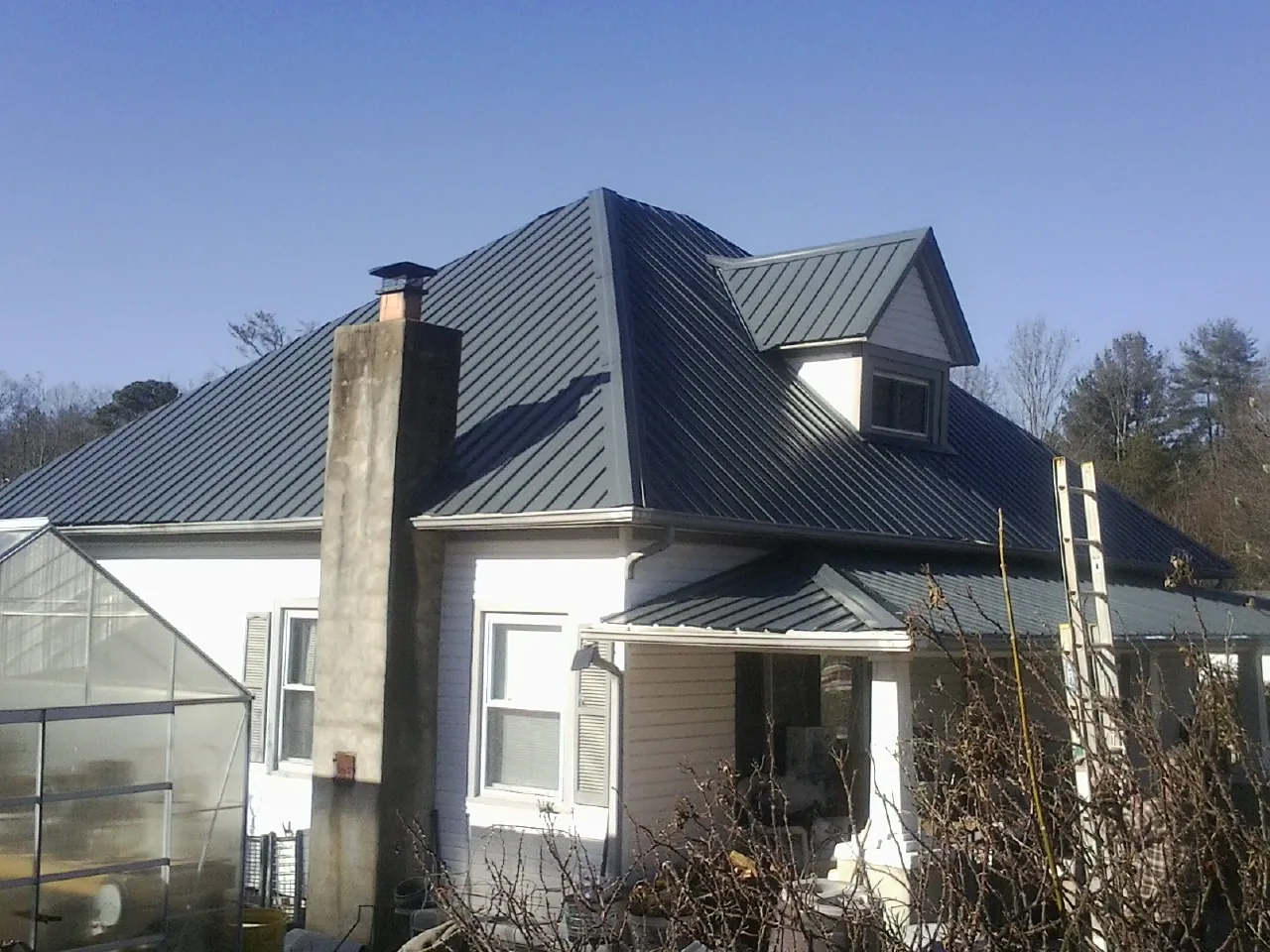 Dark blue standing seam metal roof on a white farmhouse with dormer — Slate & Tile Roof Repair by Roofing Brothers in Webster