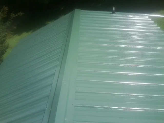 New green metal panels meeting at the ridge of a roof — Flat Roof Repair work by our crew in Webster